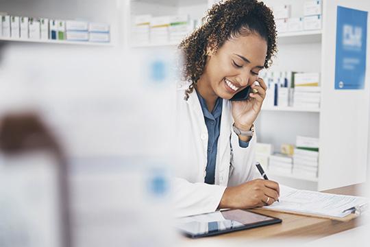 Portrait of smiling young nurse holding digital tablet with elderly patient and doctor in background at hospital. Horizontal shot.